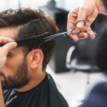 Close up of hairdresser arms cutting and combing male hair